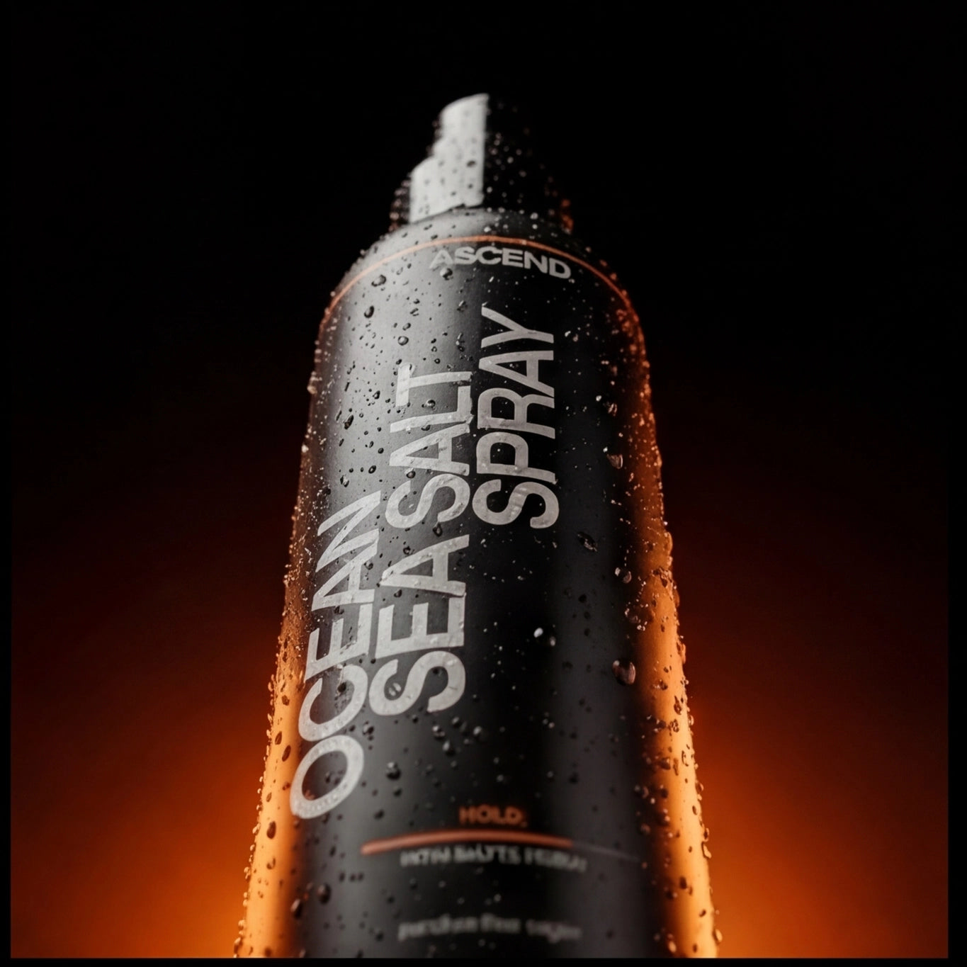 Close-up of ASCEND Ocean Salt Sea Spray bottle with water droplets against a dark, orange-lit background.