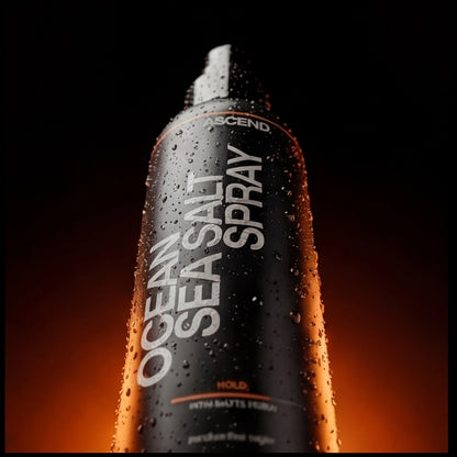 Close-up of ASCEND Ocean Salt Sea Spray bottle with water droplets against a dark, orange-lit background.