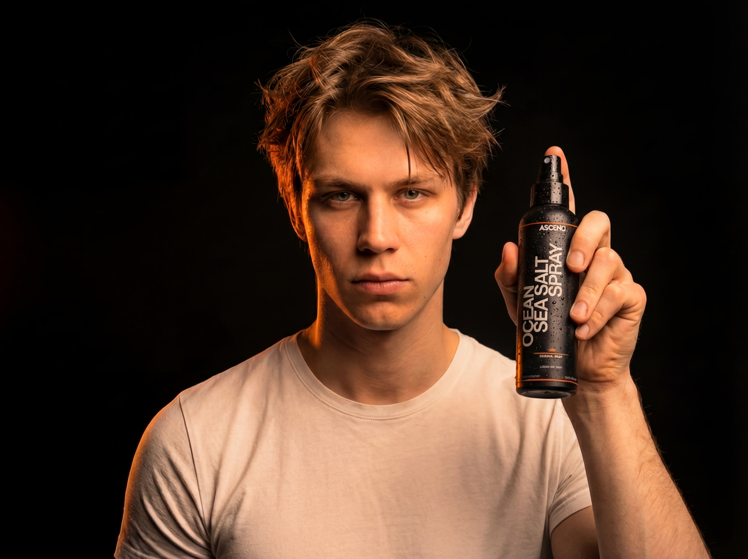 Man holding ASCEND Ocean Salt Sea Spray bottle with textured, natural-looking hair against a dark background.